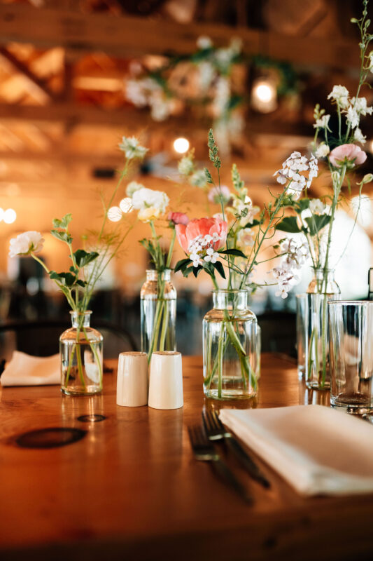 Glass bud vases filled with small white and pink flowers on a wooden table.