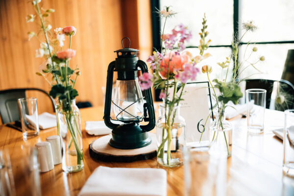 Table decorated with a black rustic style lantern in the center and surrounded by small bud vases filled with flowers.