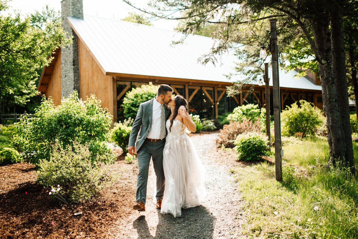 Bride and groom kissing as the walk down the path away from the events pavilion on a sunny spring day.