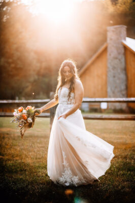 Bride twirling her dress in the field next to the events pavilion. She is basked in the glow of the setting summer sun.