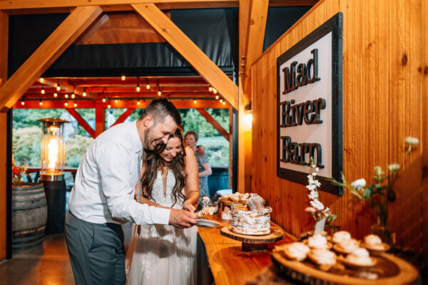 Bride and groom laughing while cutting their cake decorated to look like a birch log.