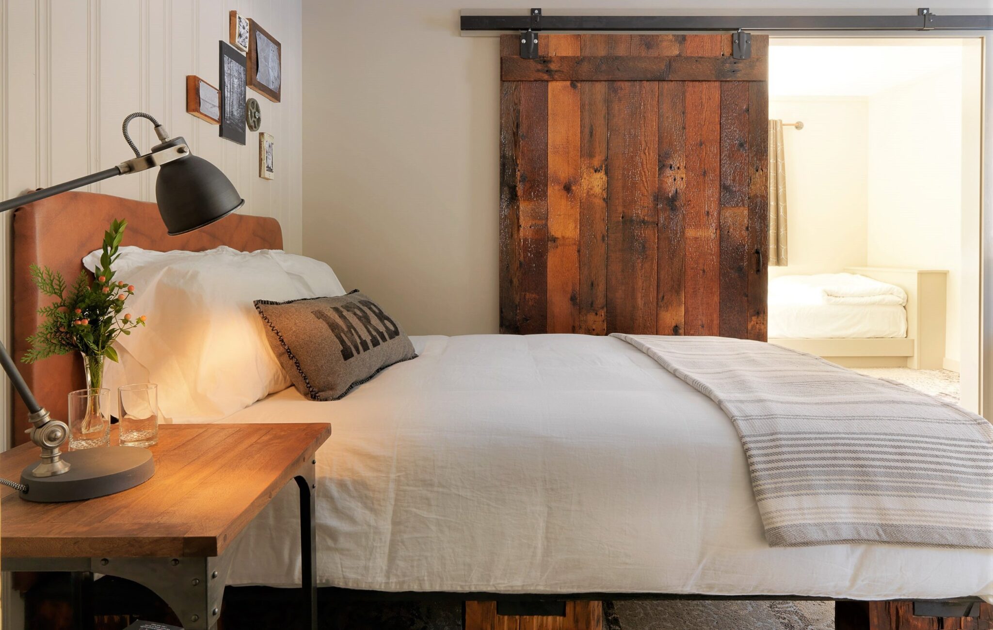 An image of the queen bed in the main room of the B5 suite in the Main Barn at the Mad River Barn Inn. A wooden sliding barn door separates the room with the 4 twin beds.