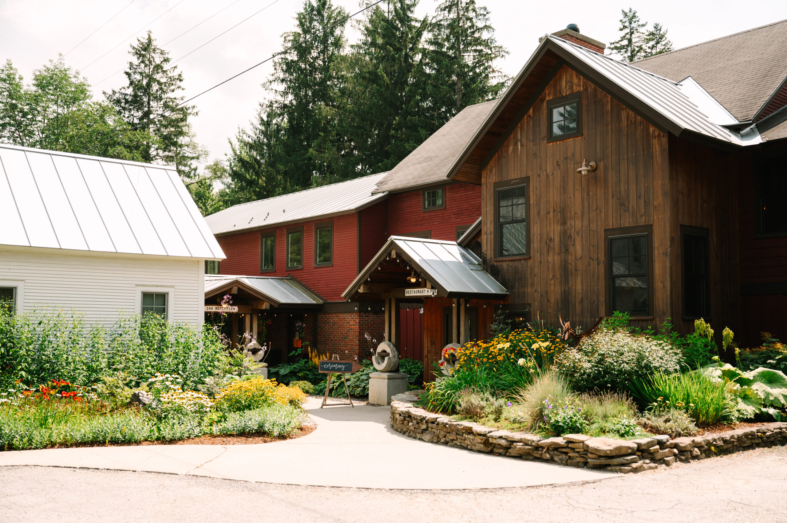 An image of the front of the Mad River Barn in Waitsfield, VT. The perennial gardens are green and lush.