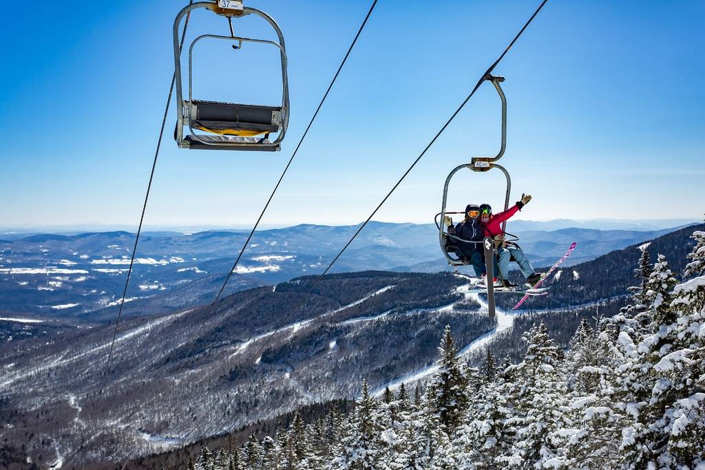 Image of two people waving to the camera while sitting on a ski lift at Sugarbush Ski Resort in Waitsfield, VT