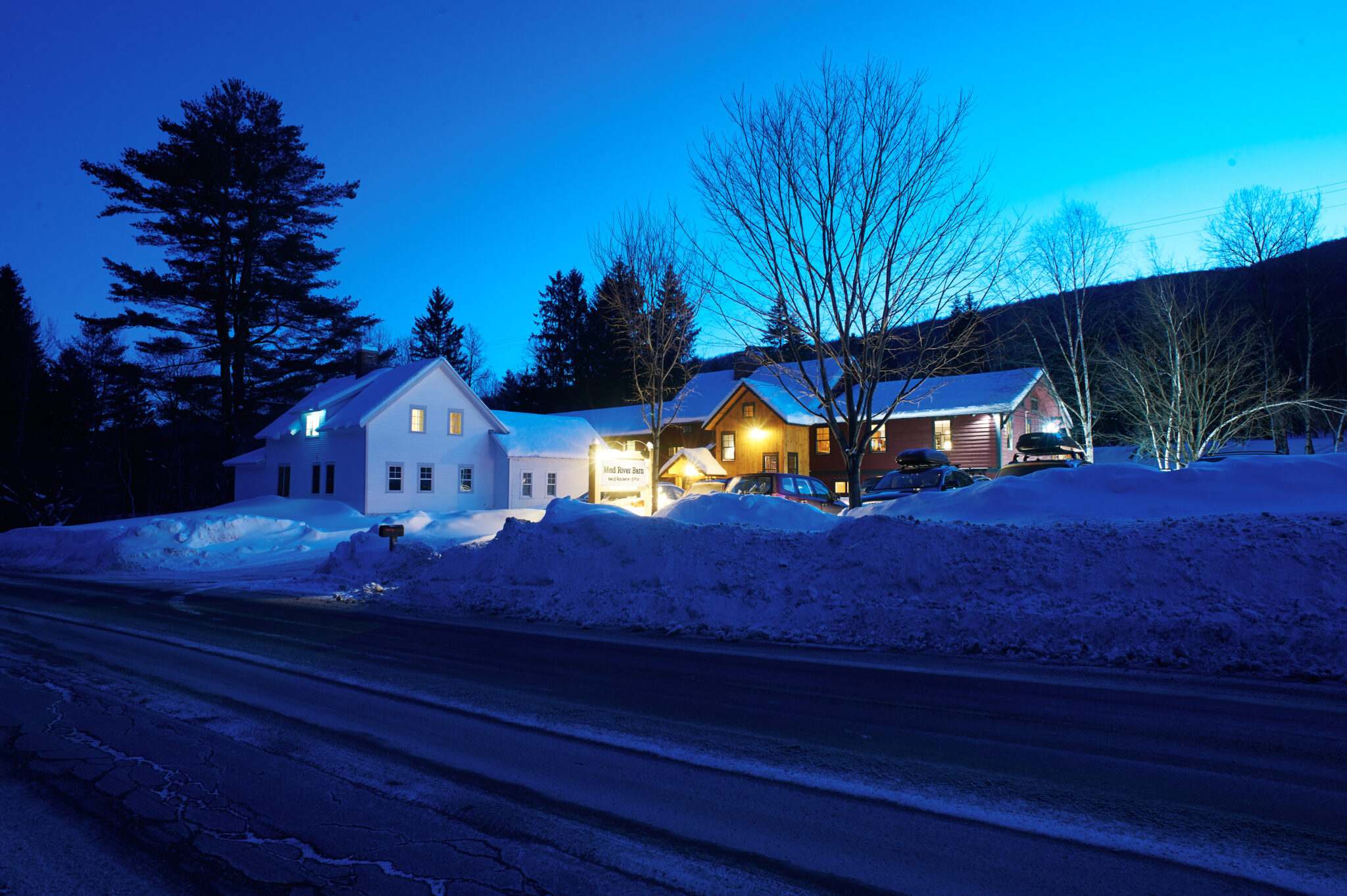 An image of the front of the Mad River Barn at night with snow banks surrounding the property