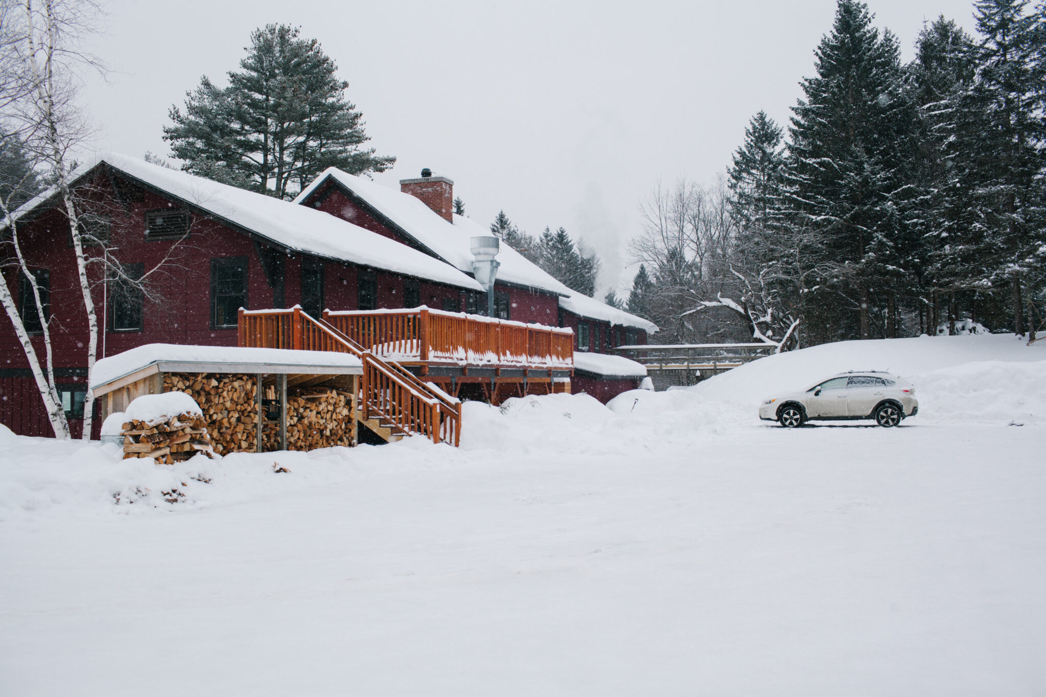 An image of the bad parking lot for the restaurant and pub of the Mad River Barn. It is snowing and the image conveys a cozy Vermont Apres vibe.